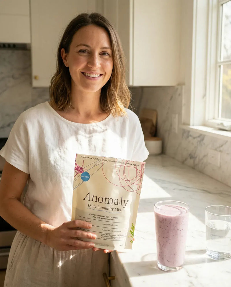 Woman holding a pouch of Anomaly Daily Immunity Mix beside a smoothie in her kitchen