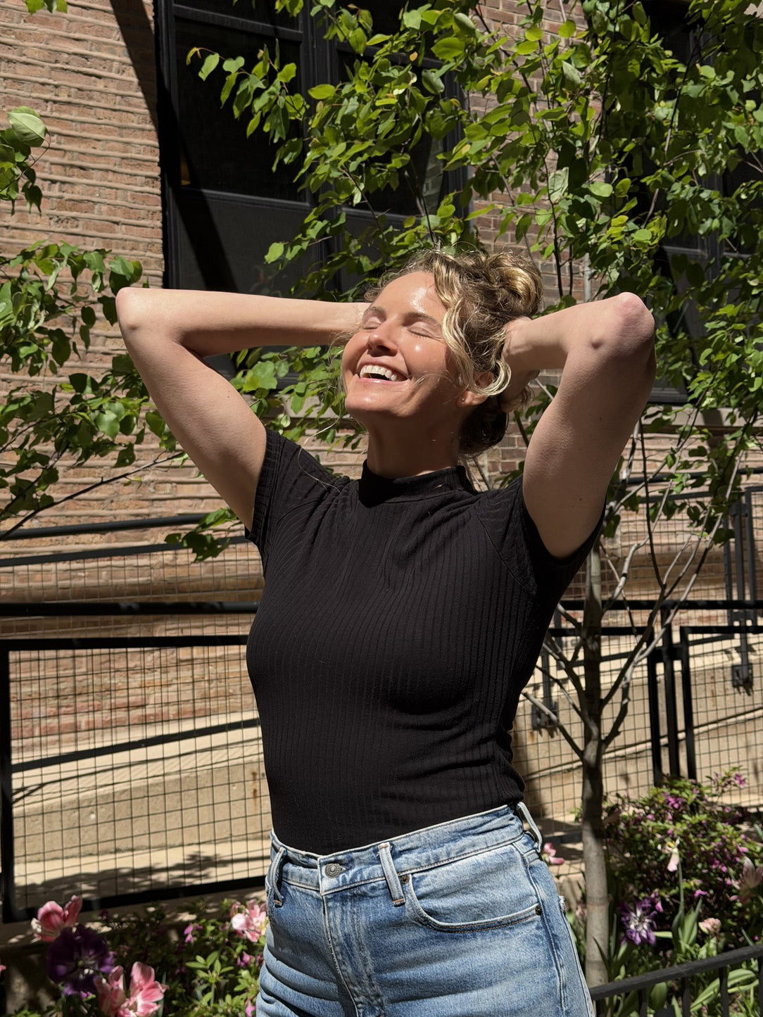 Smiling woman with her eyes closed and hands behind her head, standing in the sun